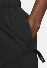 Black shorts made of lightweight material with an elastic waistband, side pockets, and a logo tag. Smooth texture with minimal stitching.