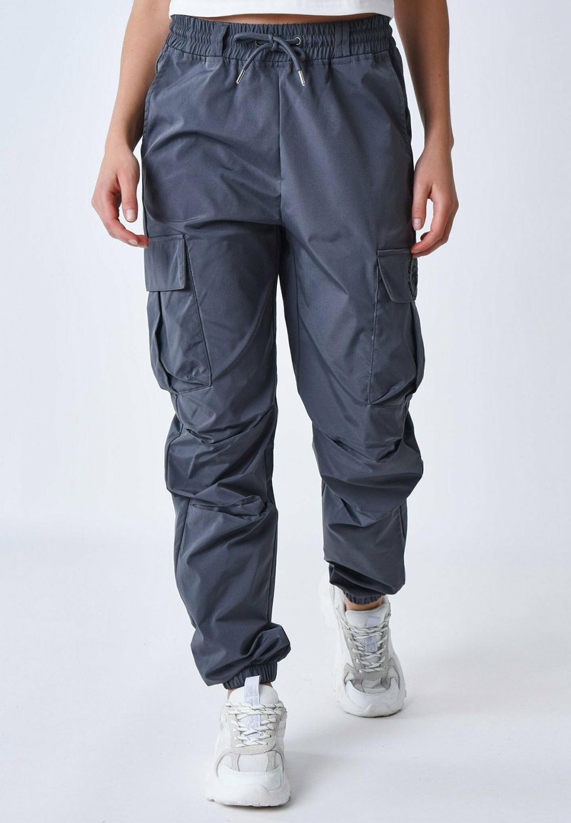 Pantaloni cargo grigi realizzati in tessuto leggero, con vita elasticizzata, numerose tasche laterali e polsini affusolati. Indossati con sneakers bianche.