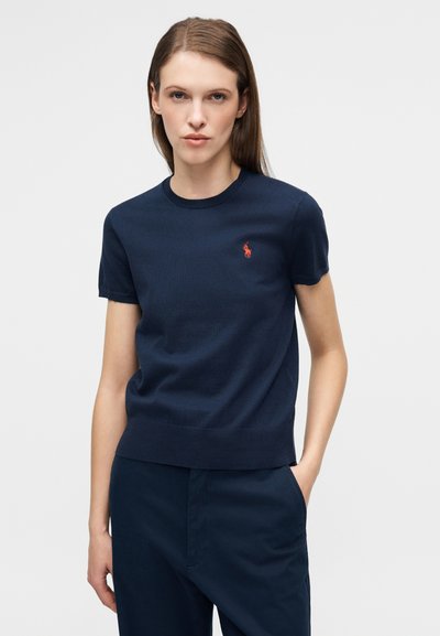 Μπλε σκούρο πουλόβερ με κοντά μανίκια και στρογγυλή λαιμόκοψη, κατασκευασμένο από απαλό πλεκτό ύφασμα, με μικρό κόκκινο λογότυπο πόλο στο πάνω αριστερό μέρος.