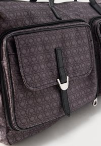 Purple patterned fabric bag with black leather strap and silver clasp on front pocket, featuring repeating abstract design.
