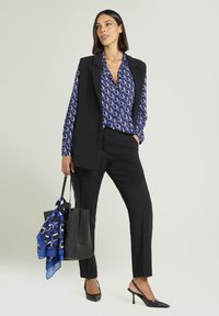 Czarne spodnie na miarę zestawione z niebieską bluzką w wzory i czarną kamizelką bez rękawów. Dodatki to czarna torba typu tote i niebieski jedwabny szalik.