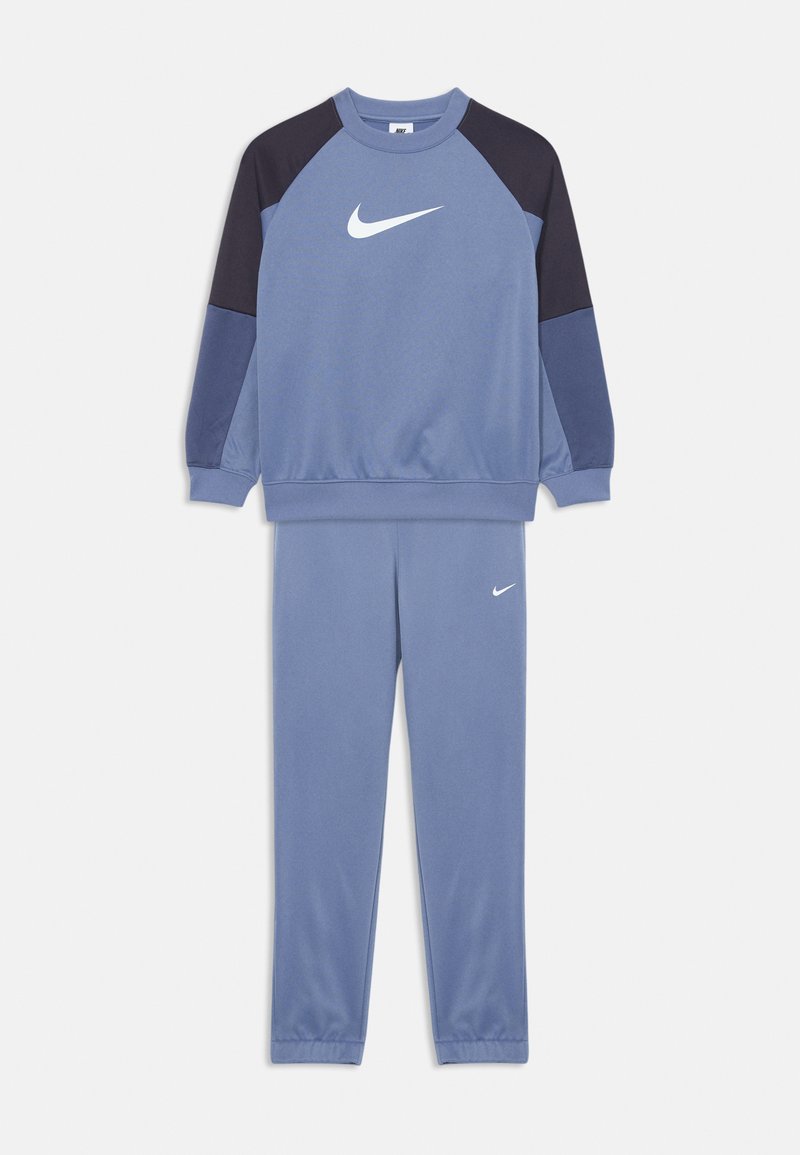 Mėlynas ir tamsiai mėlynas Nike sportinis kostiumas su baltais swoosh logotipais, kuriame yra ilgomis rankovėmis megztinis ir derančios kelnės.