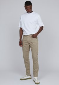 Pantalons en coton beige à coupe slim, avec une fermeture à bouton sur le devant, des passants de ceinture et des poches latérales. Associés à un t-shirt blanc à col rond et à des baskets.
