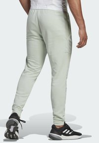 Hellgrüne Sporthose mit schlanker Passform, elastischem Bund, Seitentaschen und subtiler Textur, kombiniert mit schwarz-weißen Sneakers.