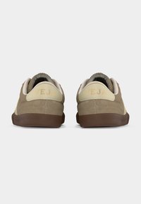 Ζευγάρι μπεζ και καφέ σουέντ αθλητικά παπούτσια με λογότυπο VEJA στη φτέρνα και καφέ λάστιχα με υφή, εμφανιζόμενα από πίσω.