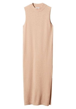 Femme portant une robe beige en maille sans manches, mains sur les hanches, sur un fond clair uni.
