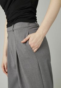 Pantalons gris au tissu lisse, dotés d'une poche latérale, d'un devant plat et de plis subtils. Assortis à un haut noir.