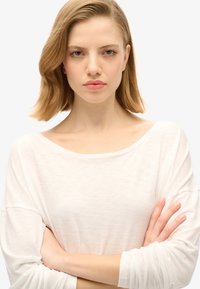 Langarm, off-white top met een wijde halslijn en relaxte pasvorm. Gemaakt van lichtgewicht stof, met opgerolde mouwen en subtiele textuur.