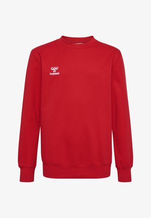 Zwei Kinder stehen, tragen rote Sweatshirts, marineblaue Hosen und weiße Turnschuhe vor einem schlichten hellen Hintergrund.