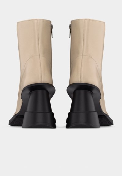Μπεζ μπότες μέχρι τη μέση της γάμπας με μαύρα χοντρά τετράγωνα τακούνια, πίσω κλείσιμο με φερμουάρ και εμφανείς ραφές σε απλό ανοιχτό φόντο.