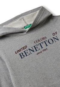 Felpa grigia con cappuccio realizzata in un materiale morbido. Presenta una scritta navale e bordeaux con la dicitura "UNITED COLORS OF BENETTON dal 1965" sulla parte anteriore.