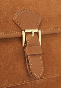 Borsa a tracolla in suede color beige con una chiusura in metallo dorato e finitura testurizzata, accompagnata da cuciture a contrasto lungo la chiusura e i bordi.