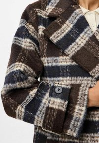 Cappotto di lana a quadri con colori marrone, blu navy e crema, dotato di colletto a ribalta e dettaglio con bottone nero sulla manica. Texture morbida.