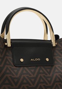 Sac à main à motif géométrique marron et noir avec une anse et des quincailleries en métal doré, comportant un accent en cuir noir avec un détail de logo.