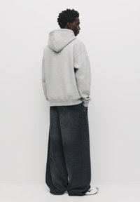 Felpa grigia con una vestibilità rilassata, dotata di un ampio cappuccio e polsini a coste, abbinata a jeans in denim scuro a vestibilità ampia.