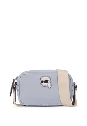 Light blue crossbody bag made of smooth material, featuring a zipper closure and a character patch with sunglasses. Includes a beige strap.