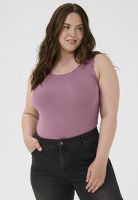 Top lavandă cu dungi, cu dantelă pe decolteu, asociat cu blugi negri din denim, o mână sprijinită în buzunar, textură netedă.