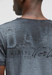 Gray, short-sleeve t-shirt with a distressed texture, featuring large black printed text and a vintage graphic design on the back.