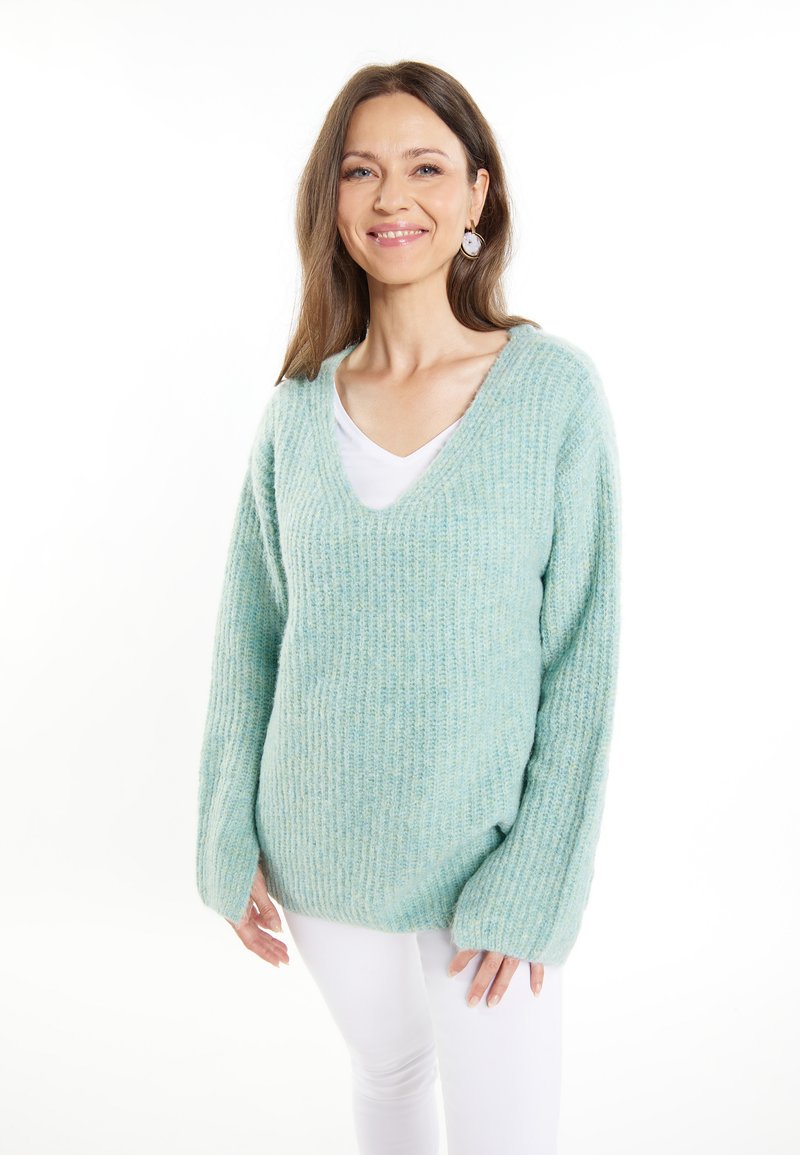 Pullover tricotat de culoare albastru deschis, cu decolteu în V, textură cu nervuri și mâneci lungi, asortat cu o cămașă albă și pantaloni albi.