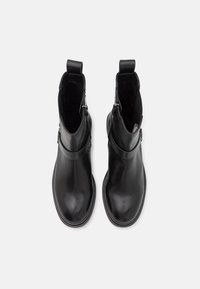 Paire de bottines en cuir noir avec fermetures éclair latérales et languettes, vues de dessus sur un fond clair.