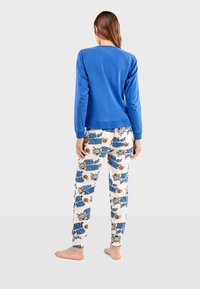 Haut à manches longues bleu avec un col rond, associé à un bas de pyjama blanc doté d'un imprimé coloré "Tom et Jerry" et d'une taille élastique.