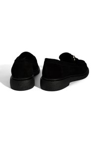 Black suede shoes with a rounded toe, low textured rubber sole, and a simple metal accent on the side. Classic slip-on design.