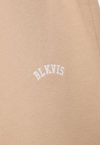 Beige bomullstoff med hvit brodert tekst som leser "BLKVIS" i en buet form. Glatt tekstur med en subtil, ensartet utseende.