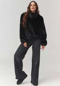 Czarna kurtka z sztucznego futra z wysokim kołnierzem i luźnym krojem, zestawiona z szerokimi, ciemnymi dżinsami. Gładka faktura i swobodna sylwetka.