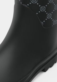 Botte de pluie en caoutchouc noir avec une surface lisse, une tige à motif gris présentant des designs circulaires, et une semelle texturée pour l'adhérence.