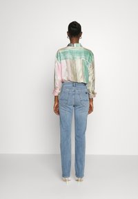 Monivärinen raidallinen silkki-paita, jossa on vihreä, vaaleanpunainen ja beige kuvio, yhdistettynä vaaleansinisiin korkeavyötäröisiin farkkuihin.