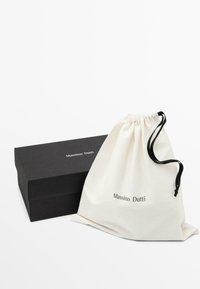Boîte rectangulaire noire de la marque Massimo Dutti à côté d'une pochette blanche à cordon avec des cordons noirs et la même marque.