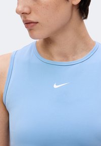 Gros plan d'une personne portant un haut sans manches Nike bleu clair avec un logo Nike blanc sur la poitrine, regardant légèrement vers la gauche.
