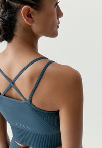 Mörkblå tränings�överdel med figursydd design, ribbad textur och korslagda axelband baktill. Diskret märkning synlig.