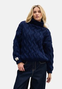 Granatowy sweter z dzianiny z wysokim kołnierzem i teksturowanym wzorem warkocza; posiada prążkowane mankiety i pasek, metka na lewej rękawie.