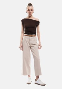 Ruskea olkapäiden yli ulottuva ribbipaita, beige leveät housut vyön kanssa ja valkoiset tennarit ruskeilla yksityiskohdilla. Suorastaan sileät tekstuurit, moderni istuvuus.