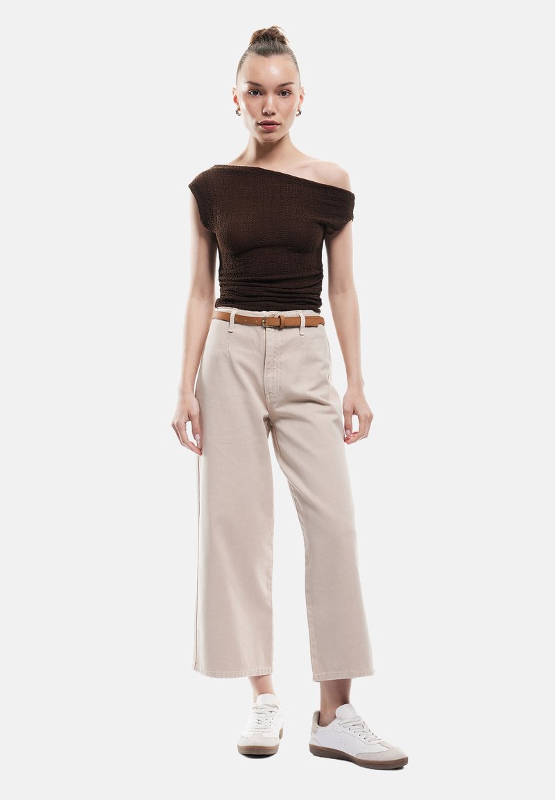 Ruskea olkapäiden yli ulottuva ribbipaita, beige leveät housut vyön kanssa ja valkoiset tennarit ruskeilla yksityiskohdilla. Suorastaan sileät tekstuurit, moderni istuvuus.