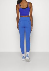 Modrý sportovní crop top a odpovídající legíny vyrobené z elastického materiálu, s přiléhavým designem a kontrastními černými popruhy nahoře.
