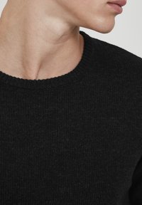 Schwarzer Strickpullover mit runder Ausschnitt, ausgestattet mit einer strukturierten Oberflächenbeschaffenheit und gerippten Bündchen. Nahaufnahme, die die Stoffdetails hervorhebt.