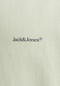 Svijetlozelena pamučna majica s tamnosivim logotipom "Jack & Jones" otisnutim sprijeda modernim, jednostavnim fontom. Glatka tekstura.