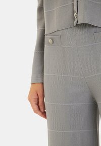 Traje gris texturizado que presenta una tela con estampado, un diseño ajustado y acentos de botones en la parte superior y la cintura de los pantalones.
