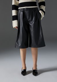 Black leather culottes with pleats and a smooth texture, paired with pointed black patent heels. The top features a black and white striped design.
