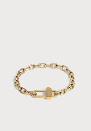 Guld kæde armbånd med store led og en rektangulær lås graveret med ordet "BOSS" på en lys baggrund.