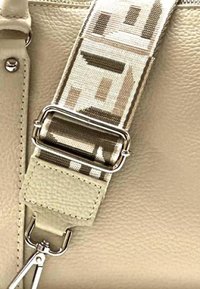 Beige leren tasdetail met een gestreepte stofriem met zilveren hardware, die geometrische vormen in gedempte tinten toont.