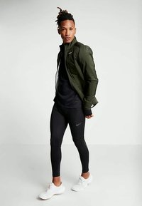 Aktiivsetele riietele mõeldud komplekt, mis sisaldab tumerohelist jakki, musta väljakujunenud särki ja musti retuuse Nike logo ning valgete spordijalatsitega.