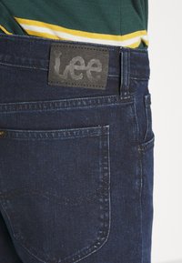 Mörkblå denimjeans med en läderpatch från Lee på midjan, med subtila sömnadsdetaljer och en sidoficka.