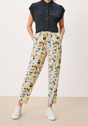Woman wearing black sleeveless button shirt with two pockets and floral tapered pants with pockets and white sneakers.