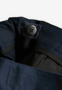 Tessuto blu navy con finitura testurizzata, dotato di un bottone nero etichettato "Clarks". Fodera interna in una tonalità nera a contrasto.