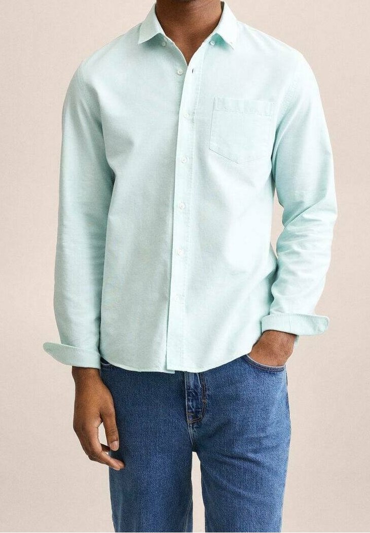 Chemise boutonnée vert menthe à manches longues, avec une poche poitrine unique et une coupe décontractée, associée à un jean bleu. Texture de tissu douce.