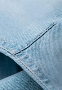 Světlá modrá deninová látka ukazující detailní záběr na švy a texturu, s hladkým povrchem a konzistentním vzorem tkaní.