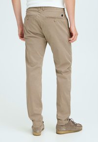 Beige chinos with a straight cut, made of cotton. Features two back pockets with button closures and a small black logo accent.